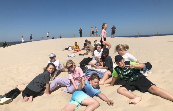 W dniach 15-18 maja 2024 roku uczniowie klas 4A i 5B wybrali się na wycieczkę do Łeby. Oto krótkie podsumowanie ich przygody.
Wizyta w Słowińskim Parku Narodowym była niezapomniana. Ruchome wydmy to unikalne miejsce, gdzie piaskowe pagórki przemieszczają się pod wpływem wiatru. Uczniowie mieli okazję spacerować po tych wydmach i podziwiać piękno natury.
W Łebie Parku czekało na nich wiele atrakcji: Zamek Strachu - dla odważnych, którzy lubią emocje; pojazdy Flinstonów - ciekawa atrakcja dla fanów kultowego serialu, Kopalnia złota - poszukiwanie skarbów; Labirynt magicznych luster - złudzenie nieskończonego lustra; zjeżdżalnie wodne 4 w 1 oraz zjeżdżalnia Boomerang - dla fanów wodnych atrakcji, zjazd na pontonach bez potrzeby przebierania się w stroje kąpielowe, wysokość ślizgu – 10 metrów; Diabelski Młyn, wysoki na 27 metrów wyposażony w 20 gondoli stoi nieopodal naszych zjeżdżalni, widok z góry zapiera dech w piersiach; park trampolin - ogromna przestrzeń, wypełniona parkourem, trampolinami, koszykówką, a także miejscem do robienia salt,  po których bezpiecznie wylądujesz na poduchę; autodrom - atrakcja którą zna niemal każdy! To must-have każdego parku rozrywki.
Uczniowie przemieszczali się po Łebie na melexach, co było wygodnym i ekscytującym środkiem transportu. Na koniec dnia uczniowie odpoczywali w Ośrodku Wypoczynkowym Fregata, gdzie mogli zrelaksować się po pełnym wrażeń dniu.
Wycieczka była udana, a uczniowie wrócili do domu z pięknymi wspomnieniami!