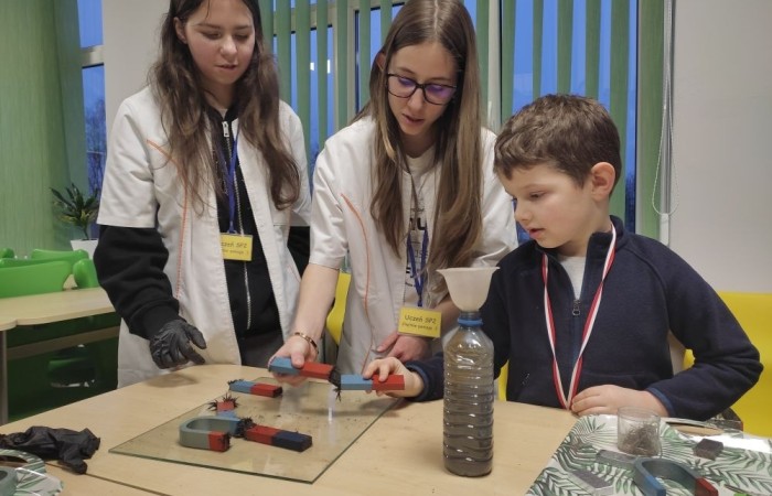 26 lutego w naszej szkole odbył się wyjątkowy DZIEŃ OTWARTY, podczas którego mieliśmy przyjemność gościć przedszkolaków, przyszłych uczniów oraz ich rodziców. Była to doskonała okazja, aby poczuć atmosferę naszej szkoły, poznać jej ofertę edukacyjną i odkryć to, co czyni ją miejscem pełnym pasji, wiedzy i radości.
Zwiedzanie naszej placówki obejmowało sale przedmiotowe, bibliotekę, stołówkę, świetlicę oraz małą salę gimnastyczną, gdzie można było na własnej skórze poczuć rytm codziennego życia naszej szkolnej społeczności.
Na odwiedzających czekało mnóstwo niespodzianek! Zachętą do działania były pieczątki, które najmłodsi otrzymywali w nagrodę za wykonanie przeróżnych zadań. W sali gimnastycznej na uczestników czekały ekscytujące konkurencje sprawnościowe, a w pracowni kulinarnej – pachnące i chrupiące gofry własnej roboty. Młodzi odkrywcy mieli okazję badać świat przez mikroskop, eksperymentować z interaktywnymi robotami Photon oraz brać udział w zajęciach z robotyki. Z kolei miłośnicy sztuki mogli tworzyć piękne dzieła na warsztatach plastycznych i origami, a najmłodsi cieszyli się malowaniem twarzy.
Nie zabrakło także wyzwań dla bystrego umysłu! Gry i zabawy językowe, rebusy oraz polonistyczne łamigłówki rozbudzały wyobraźnię i rozwijały umiejętności językowe. Wesoła „Gimnastyka buzi i języka” sprawiła, że ćwiczenie dykcji stało się czystą przyjemnością. Ogromnym zainteresowaniem cieszyły się również gry planszowe, które dostarczyły mnóstwa radości i emocjonującej rywalizacji. Dodatkowo, zabawy z chustą Klanza okazały się świetnym sposobem na integrację i wspólną zabawę pełną śmiechu.
Aktywne zwiedzanie stało się więc okazją do rozwijania ciekawości świata, nabywania nowych umiejętności, pobudzania w najmłodszych kreatywności oraz odczuwania satysfakcji z osiągniętego sukcesu.