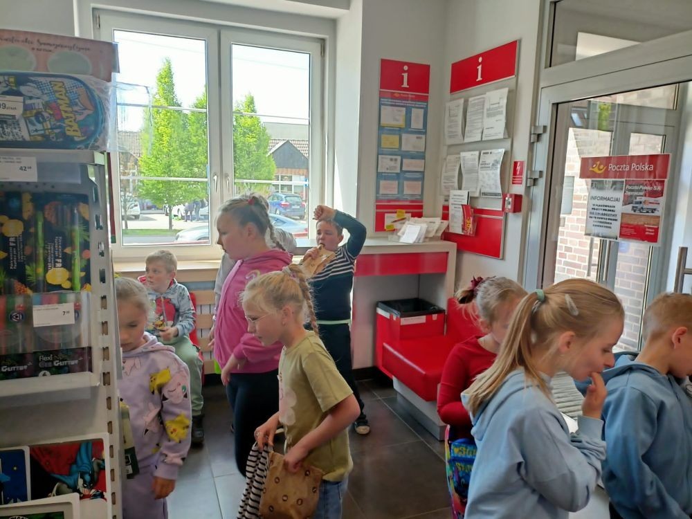 W piątek uczniowie klasy 1a wybrali się na wyjątkową wycieczkę do pobliskiego urzędu pocztowego. Dzieci miały okazję z bliska przyjrzeć się pracy pocztowców, dowiedzieć się, jak wygląda droga listu od nadawcy do adresata, a także zobaczyć, jak działa okienko pocztowe czy stemplowanie przesyłek. Najważniejszym punktem wizyty było jednak coś naprawdę wyjątkowego – uczniowie samodzielnie wysłali listy-niespodzianki z okazji Dnia Mamy. Każda koperta kryła w sobie serce pełne miłości i wdzięczności dla najważniejszych osób w ich życiu.