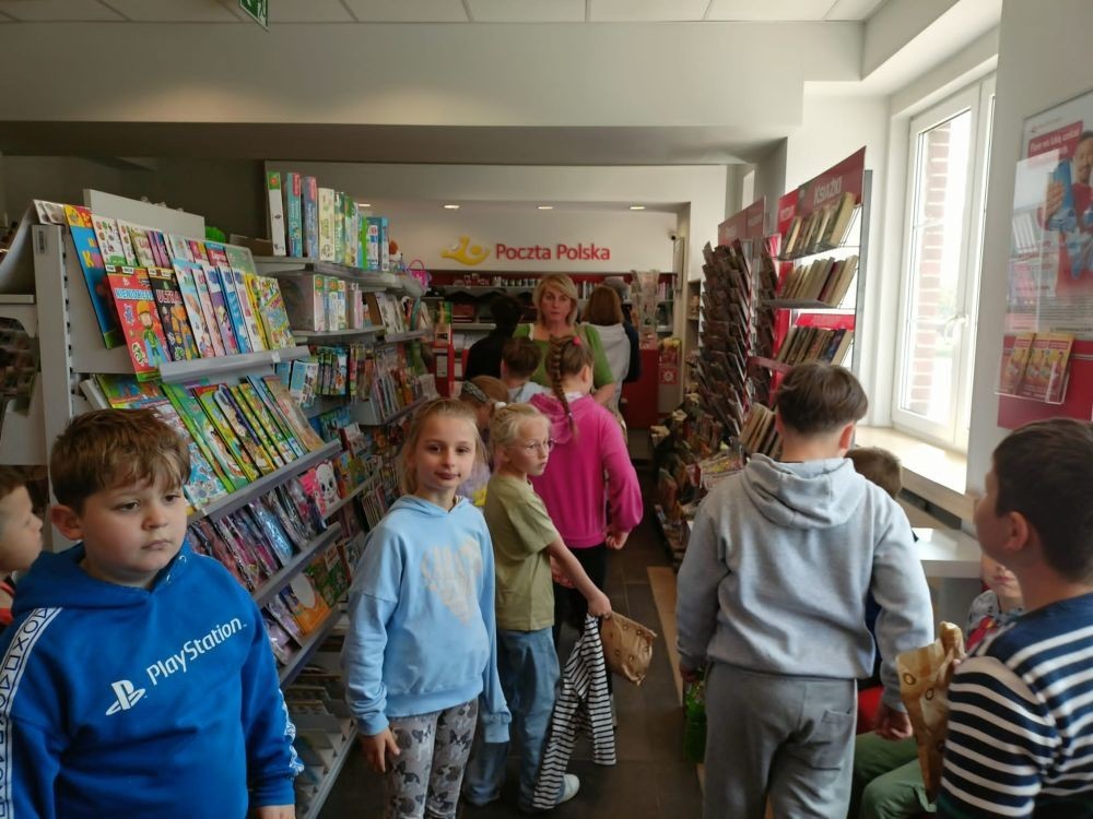 W piątek uczniowie klasy 1a wybrali się na wyjątkową wycieczkę do pobliskiego urzędu pocztowego. Dzieci miały okazję z bliska przyjrzeć się pracy pocztowców, dowiedzieć się, jak wygląda droga listu od nadawcy do adresata, a także zobaczyć, jak działa okienko pocztowe czy stemplowanie przesyłek. Najważniejszym punktem wizyty było jednak coś naprawdę wyjątkowego – uczniowie samodzielnie wysłali listy-niespodzianki z okazji Dnia Mamy. Każda koperta kryła w sobie serce pełne miłości i wdzięczności dla najważniejszych osób w ich życiu.