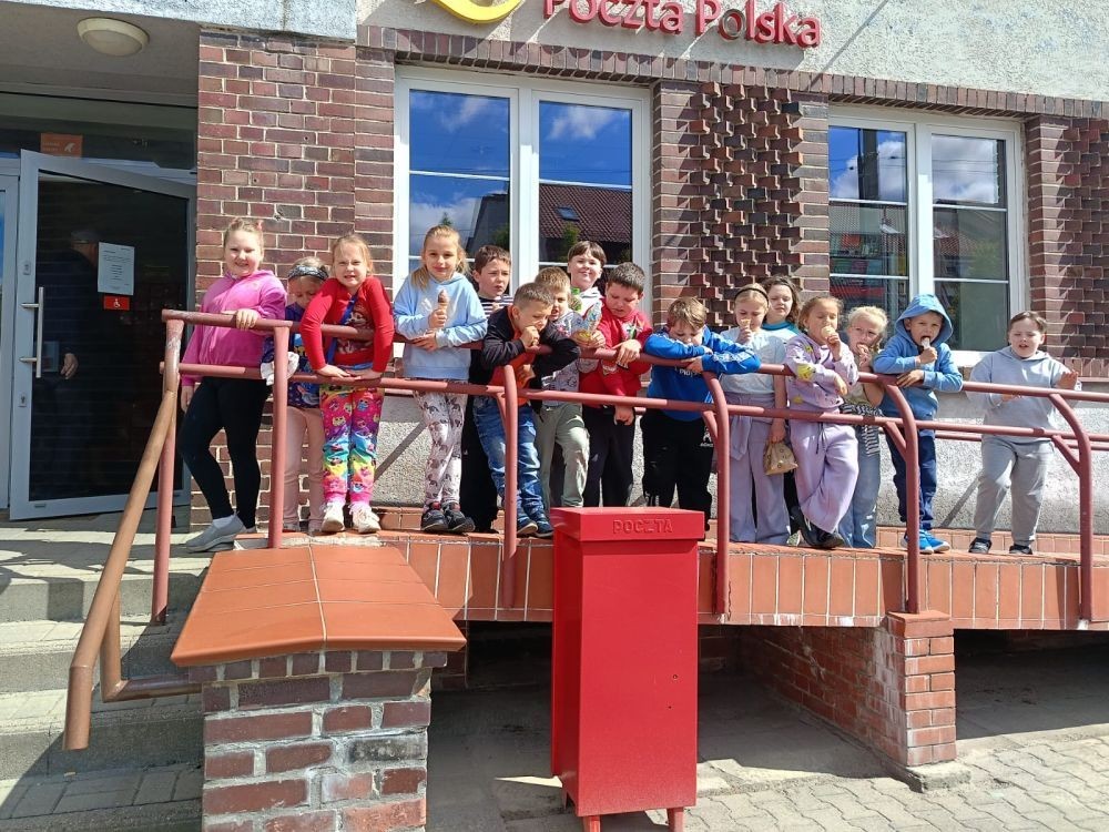 W piątek uczniowie klasy 1a wybrali się na wyjątkową wycieczkę do pobliskiego urzędu pocztowego. Dzieci miały okazję z bliska przyjrzeć się pracy pocztowców, dowiedzieć się, jak wygląda droga listu od nadawcy do adresata, a także zobaczyć, jak działa okienko pocztowe czy stemplowanie przesyłek. Najważniejszym punktem wizyty było jednak coś naprawdę wyjątkowego – uczniowie samodzielnie wysłali listy-niespodzianki z okazji Dnia Mamy. Każda koperta kryła w sobie serce pełne miłości i wdzięczności dla najważniejszych osób w ich życiu.