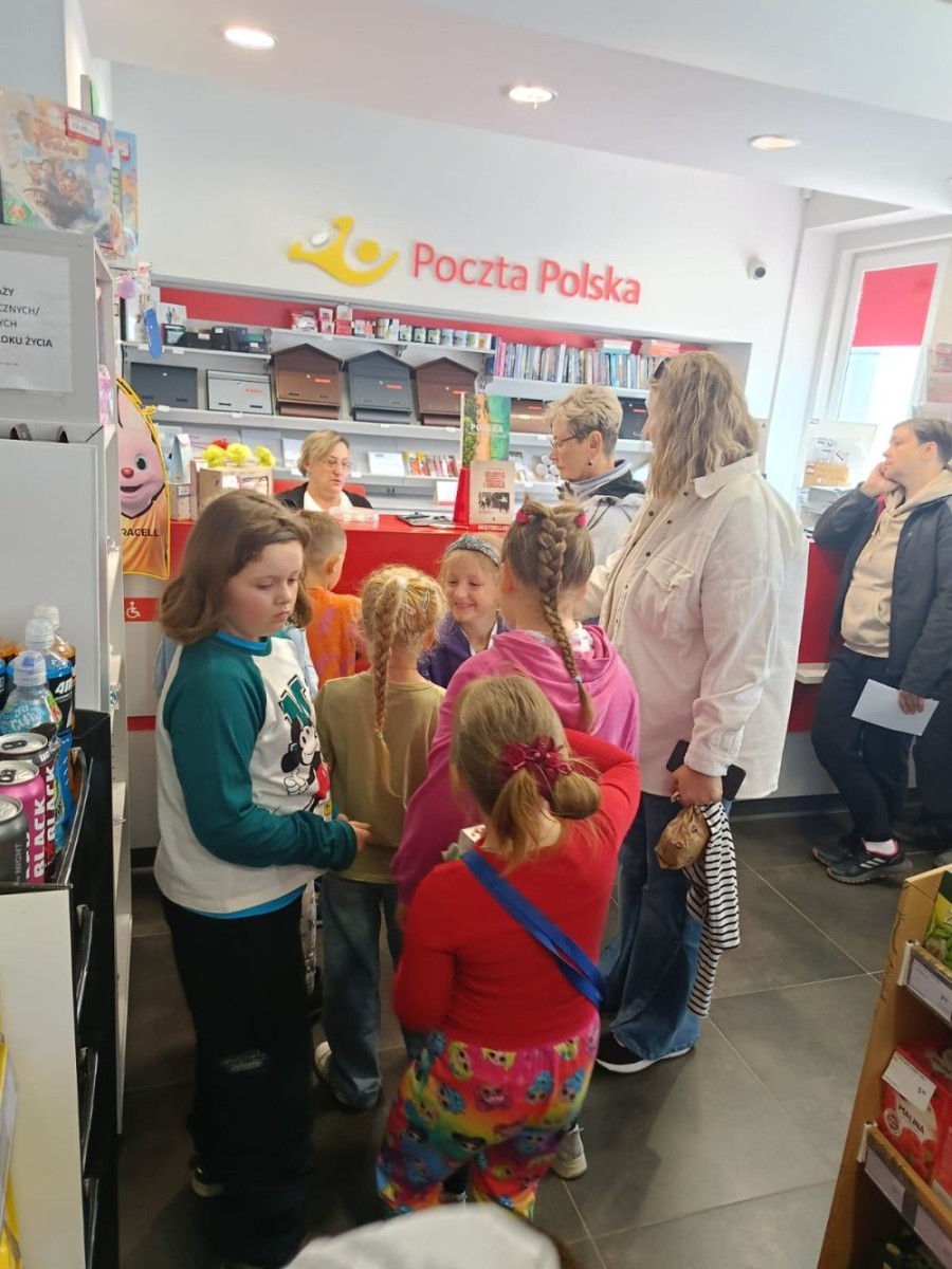 W piątek uczniowie klasy 1a wybrali się na wyjątkową wycieczkę do pobliskiego urzędu pocztowego. Dzieci miały okazję z bliska przyjrzeć się pracy pocztowców, dowiedzieć się, jak wygląda droga listu od nadawcy do adresata, a także zobaczyć, jak działa okienko pocztowe czy stemplowanie przesyłek. Najważniejszym punktem wizyty było jednak coś naprawdę wyjątkowego – uczniowie samodzielnie wysłali listy-niespodzianki z okazji Dnia Mamy. Każda koperta kryła w sobie serce pełne miłości i wdzięczności dla najważniejszych osób w ich życiu.
