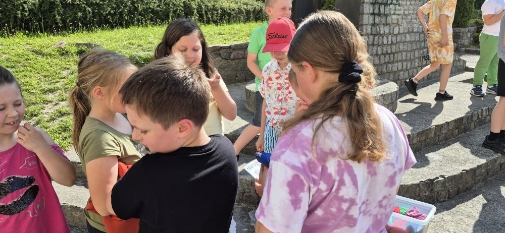 Dziś uczniowie klasy 2b wybrali się na plac przed szkołę, gdzie połączyli przyjemne z pożytecznym. Podczas zabawy w rzuty woreczkiem do celu dzieci nie tylko świetnie się bawiły, ale również ćwiczyły swoją sprawność rachunkową – dodając zdobyte przez grupy punkty.  Radość, ruch i nauka w jednym – właśnie tak lubimy się uczyć.