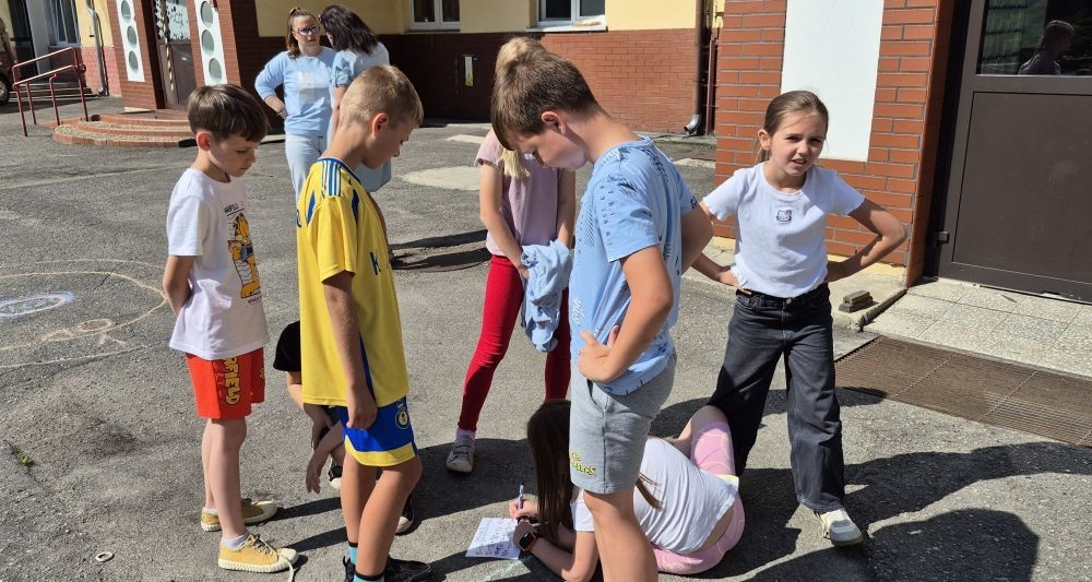 Dziś uczniowie klasy 2b wybrali się na plac przed szkołę, gdzie połączyli przyjemne z pożytecznym. Podczas zabawy w rzuty woreczkiem do celu dzieci nie tylko świetnie się bawiły, ale również ćwiczyły swoją sprawność rachunkową – dodając zdobyte przez grupy punkty.  Radość, ruch i nauka w jednym – właśnie tak lubimy się uczyć.