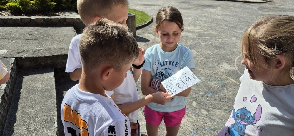 Dziś uczniowie klasy 2b wybrali się na plac przed szkołę, gdzie połączyli przyjemne z pożytecznym. Podczas zabawy w rzuty woreczkiem do celu dzieci nie tylko świetnie się bawiły, ale również ćwiczyły swoją sprawność rachunkową – dodając zdobyte przez grupy punkty.  Radość, ruch i nauka w jednym – właśnie tak lubimy się uczyć.