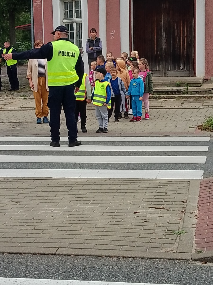 Dzieci z grup starszych Sówki, Leśne skrzaty oraz Biedronki odwiedzili funkcjonariusze policji drogowej , którzy przeprowadzili zajęcia edukacyjne na temat bezpieczeństwa w ruchu ulicznym. Wydarzenie odbyło się w ramach zajęć ,,Moja droga do przedszkola”, której celem jest kształtowanie prawidłowych nawyków i świadomości wśród najmłodszych uczestników ruchu drogowego. Policjanci opowiedzieli przedszkolakom o zasadach bezpiecznego przechodzenia przez jezdnię, znaczeniu znaków drogowych. Dzieci dowiedziały się również, dlaczego ważne jest noszenie odblasków, zwłaszcza jesienią i zimą, gdy wcześniej zapada zmrok.                                
Takie spotkania są bardzo ważne. Dzieci w tym wieku chłoną wiedzę jak gąbka.                  Warto więc już teraz uczyć je zasad, które mogą uratować życie. Przedszkolaki pożegnały policjanta gromkimi brawami i obiecały zawsze pamiętać o zasadach bezpieczeństwa.
Spotkanie z policjantem było nie tylko cenną lekcją, ale też okazją do wzbudzenia w dzieciach zaufania do funkcjonariuszy. To ważny krok w budowaniu poczucia bezpieczeństwa od najmłodszych lat.
