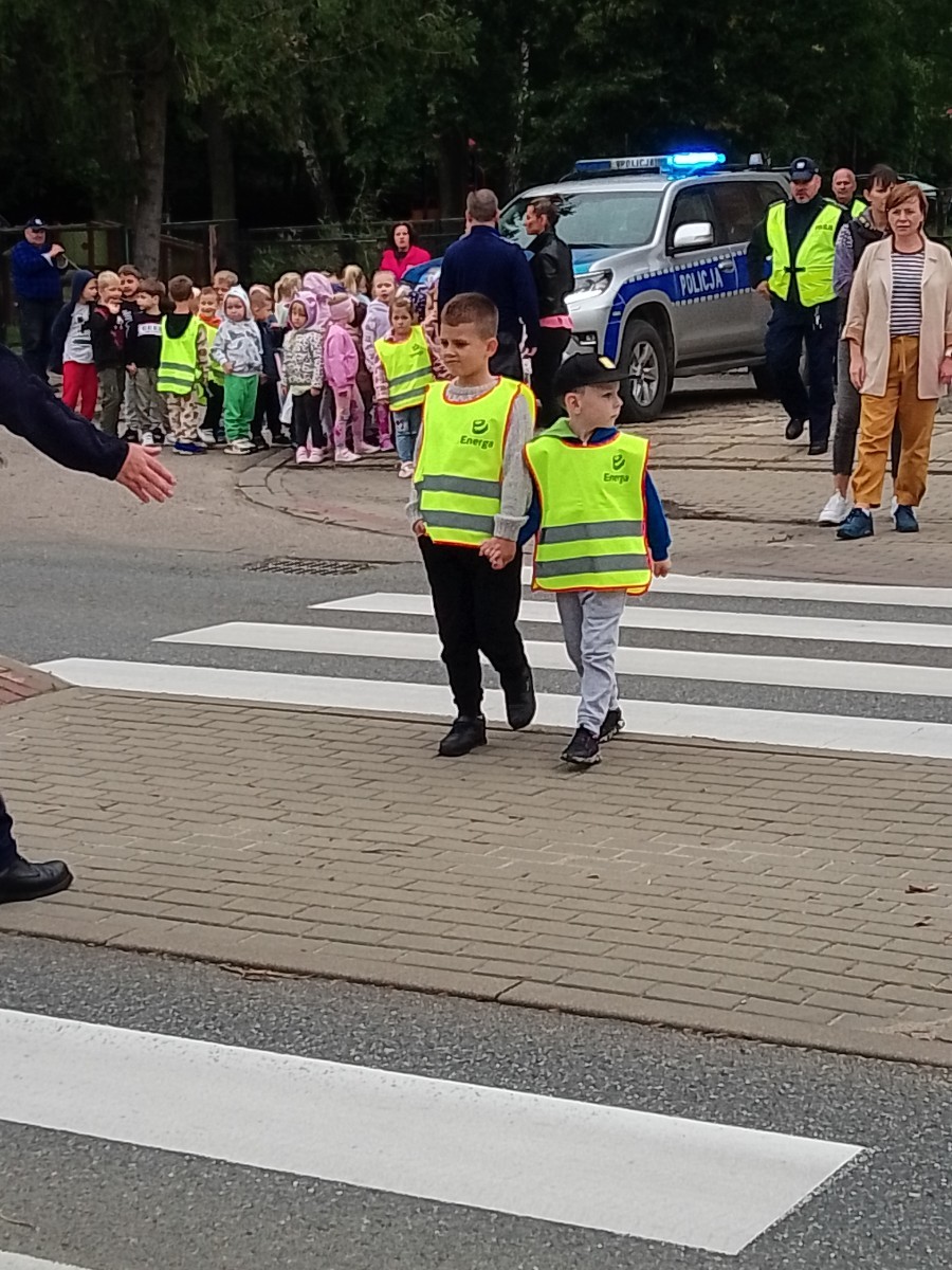 Dzieci z grup starszych Sówki, Leśne skrzaty oraz Biedronki odwiedzili funkcjonariusze policji drogowej , którzy przeprowadzili zajęcia edukacyjne na temat bezpieczeństwa w ruchu ulicznym. Wydarzenie odbyło się w ramach zajęć ,,Moja droga do przedszkola”, której celem jest kształtowanie prawidłowych nawyków i świadomości wśród najmłodszych uczestników ruchu drogowego. Policjanci opowiedzieli przedszkolakom o zasadach bezpiecznego przechodzenia przez jezdnię, znaczeniu znaków drogowych. Dzieci dowiedziały się również, dlaczego ważne jest noszenie odblasków, zwłaszcza jesienią i zimą, gdy wcześniej zapada zmrok.                                
Takie spotkania są bardzo ważne. Dzieci w tym wieku chłoną wiedzę jak gąbka.                  Warto więc już teraz uczyć je zasad, które mogą uratować życie. Przedszkolaki pożegnały policjanta gromkimi brawami i obiecały zawsze pamiętać o zasadach bezpieczeństwa.
Spotkanie z policjantem było nie tylko cenną lekcją, ale też okazją do wzbudzenia w dzieciach zaufania do funkcjonariuszy. To ważny krok w budowaniu poczucia bezpieczeństwa od najmłodszych lat.
