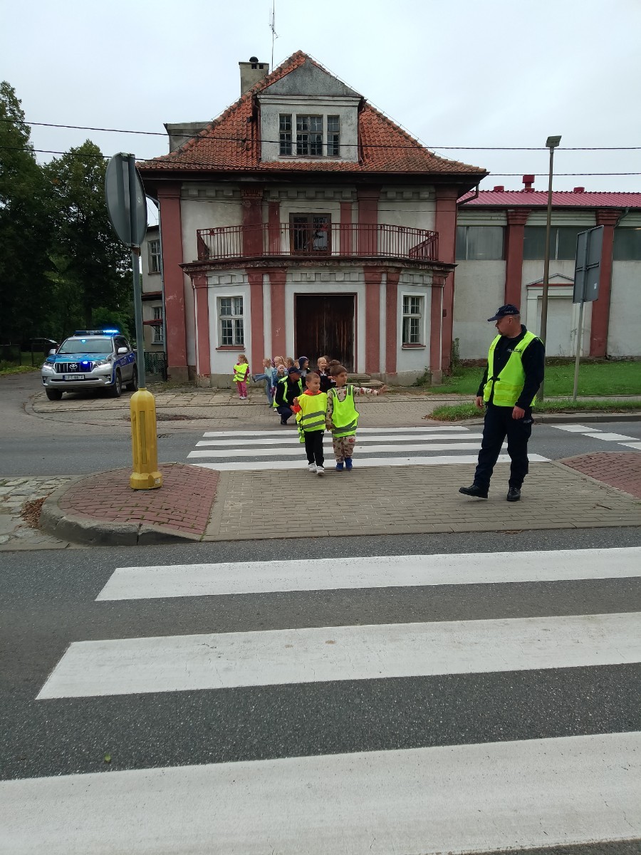 Dzieci z grup starszych Sówki, Leśne skrzaty oraz Biedronki odwiedzili funkcjonariusze policji drogowej , którzy przeprowadzili zajęcia edukacyjne na temat bezpieczeństwa w ruchu ulicznym. Wydarzenie odbyło się w ramach zajęć ,,Moja droga do przedszkola”, której celem jest kształtowanie prawidłowych nawyków i świadomości wśród najmłodszych uczestników ruchu drogowego. Policjanci opowiedzieli przedszkolakom o zasadach bezpiecznego przechodzenia przez jezdnię, znaczeniu znaków drogowych. Dzieci dowiedziały się również, dlaczego ważne jest noszenie odblasków, zwłaszcza jesienią i zimą, gdy wcześniej zapada zmrok.                                
Takie spotkania są bardzo ważne. Dzieci w tym wieku chłoną wiedzę jak gąbka.                  Warto więc już teraz uczyć je zasad, które mogą uratować życie. Przedszkolaki pożegnały policjanta gromkimi brawami i obiecały zawsze pamiętać o zasadach bezpieczeństwa.
Spotkanie z policjantem było nie tylko cenną lekcją, ale też okazją do wzbudzenia w dzieciach zaufania do funkcjonariuszy. To ważny krok w budowaniu poczucia bezpieczeństwa od najmłodszych lat.
