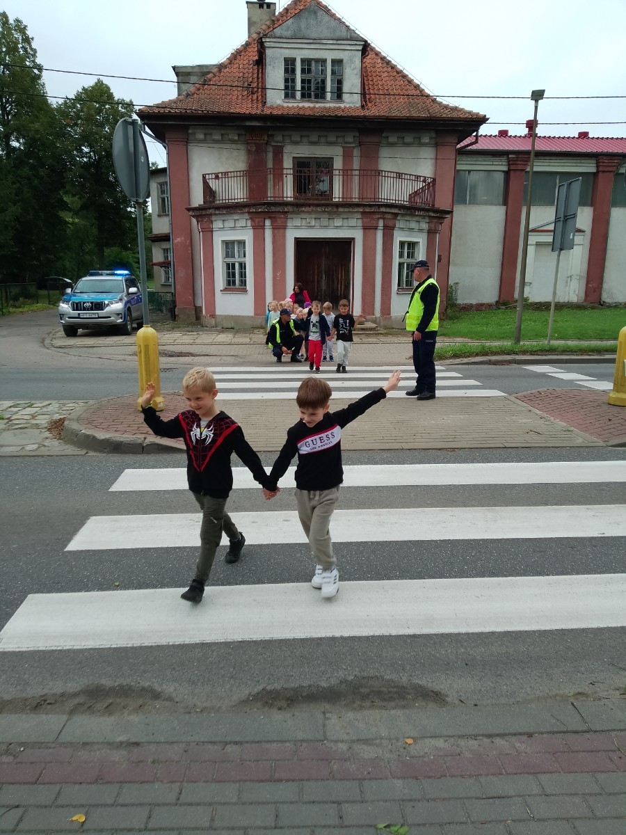 Dzieci z grup starszych Sówki, Leśne skrzaty oraz Biedronki odwiedzili funkcjonariusze policji drogowej , którzy przeprowadzili zajęcia edukacyjne na temat bezpieczeństwa w ruchu ulicznym. Wydarzenie odbyło się w ramach zajęć ,,Moja droga do przedszkola”, której celem jest kształtowanie prawidłowych nawyków i świadomości wśród najmłodszych uczestników ruchu drogowego. Policjanci opowiedzieli przedszkolakom o zasadach bezpiecznego przechodzenia przez jezdnię, znaczeniu znaków drogowych. Dzieci dowiedziały się również, dlaczego ważne jest noszenie odblasków, zwłaszcza jesienią i zimą, gdy wcześniej zapada zmrok.                                
Takie spotkania są bardzo ważne. Dzieci w tym wieku chłoną wiedzę jak gąbka.                  Warto więc już teraz uczyć je zasad, które mogą uratować życie. Przedszkolaki pożegnały policjanta gromkimi brawami i obiecały zawsze pamiętać o zasadach bezpieczeństwa.
Spotkanie z policjantem było nie tylko cenną lekcją, ale też okazją do wzbudzenia w dzieciach zaufania do funkcjonariuszy. To ważny krok w budowaniu poczucia bezpieczeństwa od najmłodszych lat.
