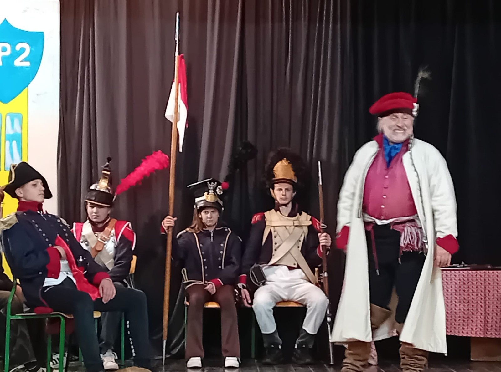 Każdego roku uczniowie naszej szkoły mają niepowtarzalną okazję wziąć udział w wyjątkowym wydarzeniu edukacyjnym - ŻYWEJ LEKCJI HISTORII, prowadzonej przez grupę rekonstrukcyjną Chorągiew Komturstwa Gniewskiego. To spotkanie, które na długo pozostaje w pamięci uczestników, łącząc wiedzę historyczną z emocjami, ruchem i bezpośrednim kontaktem z przeszłością.
W tym roku tematyka spotkań została zrealizowana na dwóch poziomach wiekowych:
Klasy 4-6: Świat starożytnych Greków i Rzymian
Uczniowie klas młodszych przenieśli się do czasów starożytności - epoki potężnych cywilizacji, mitologii, igrzysk olimpijskich i legionów rzymskich. Dzięki strojom z epoki, realistycznym rekwizytom i barwnym opowieściom rekonstruktorów, dzieci mogły poczuć atmosferę antycznego świata. Dowiedzieli się, jak wyglądało życie codzienne Greków i Rzymian, jakie były zwyczaje wojenne, a nawet jak wyglądały ćwiczenia wojskowe legionistów. Zajęcia - prowadzone w formie interaktywnej - dały uczniom możliwość przymierzenia elementów uzbrojenia oraz wzięcia udziału w krótkich pokazach.
Klasy 7-8: Długi wiek XIX
Starsze klasy uczestniczyły w lekcji poświęconej Długiemu wiekowi XIX, czyli okresowi, który ukształtował współczesny świat. Rekonstruktorzy przybliżyli wydarzenia związane z rewolucjami, walką o niepodległość, przemianami społecznymi i narodzinami nowoczesnych idei. Szczególną uwagę poświęcono wydarzeniom ważnym dla Polski - rozbiorom, powstaniom narodowym i postaciom kluczowym dla naszej historii. Uczniowie mogli zobaczyć repliki broni, a także stroje z XIX wieku. Dla wielu była to okazja do poznania historii w sposób bardziej angażujący niż podręcznik - przez opowieści, prezentacje multimedialne i inscenizacje.
Żywa lekcja historii to nie tylko atrakcja, ale przede wszystkim cenna forma nauki. Bezpośredni kontakt z pasjonatami historii oraz aktywne uczestnictwo w przedsięwzięciu sprawia, że uczniowie lepiej zapamiętują materiał, rozbudzają swoją ciekawość i rozwijają szacunek do dziedzictwa kulturowego.