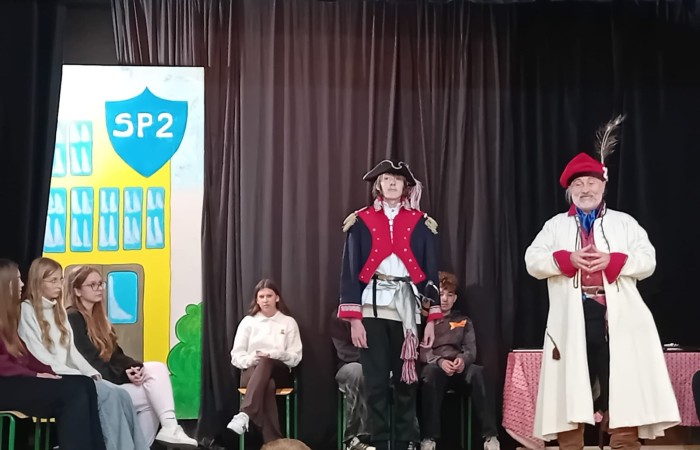 Każdego roku uczniowie naszej szkoły mają niepowtarzalną okazję wziąć udział w wyjątkowym wydarzeniu edukacyjnym - ŻYWEJ LEKCJI HISTORII, prowadzonej przez grupę rekonstrukcyjną Chorągiew Komturstwa Gniewskiego. To spotkanie, które na długo pozostaje w pamięci uczestników, łącząc wiedzę historyczną z emocjami, ruchem i bezpośrednim kontaktem z przeszłością.
W tym roku tematyka spotkań została zrealizowana na dwóch poziomach wiekowych:
Klasy 4-6: Świat starożytnych Greków i Rzymian
Uczniowie klas młodszych przenieśli się do czasów starożytności - epoki potężnych cywilizacji, mitologii, igrzysk olimpijskich i legionów rzymskich. Dzięki strojom z epoki, realistycznym rekwizytom i barwnym opowieściom rekonstruktorów, dzieci mogły poczuć atmosferę antycznego świata. Dowiedzieli się, jak wyglądało życie codzienne Greków i Rzymian, jakie były zwyczaje wojenne, a nawet jak wyglądały ćwiczenia wojskowe legionistów. Zajęcia - prowadzone w formie interaktywnej - dały uczniom możliwość przymierzenia elementów uzbrojenia oraz wzięcia udziału w krótkich pokazach.
Klasy 7-8: Długi wiek XIX
Starsze klasy uczestniczyły w lekcji poświęconej Długiemu wiekowi XIX, czyli okresowi, który ukształtował współczesny świat. Rekonstruktorzy przybliżyli wydarzenia związane z rewolucjami, walką o niepodległość, przemianami społecznymi i narodzinami nowoczesnych idei. Szczególną uwagę poświęcono wydarzeniom ważnym dla Polski - rozbiorom, powstaniom narodowym i postaciom kluczowym dla naszej historii. Uczniowie mogli zobaczyć repliki broni, a także stroje z XIX wieku. Dla wielu była to okazja do poznania historii w sposób bardziej angażujący niż podręcznik - przez opowieści, prezentacje multimedialne i inscenizacje.
Żywa lekcja historii to nie tylko atrakcja, ale przede wszystkim cenna forma nauki. Bezpośredni kontakt z pasjonatami historii oraz aktywne uczestnictwo w przedsięwzięciu sprawia, że uczniowie lepiej zapamiętują materiał, rozbudzają swoją ciekawość i rozwijają szacunek do dziedzictwa kulturowego.