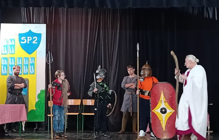 Każdego roku uczniowie naszej szkoły mają niepowtarzalną okazję wziąć udział w wyjątkowym wydarzeniu edukacyjnym - ŻYWEJ LEKCJI HISTORII, prowadzonej przez grupę rekonstrukcyjną Chorągiew Komturstwa Gniewskiego. To spotkanie, które na długo pozostaje w pamięci uczestników, łącząc wiedzę historyczną z emocjami, ruchem i bezpośrednim kontaktem z przeszłością.
W tym roku tematyka spotkań została zrealizowana na dwóch poziomach wiekowych:
Klasy 4-6: Świat starożytnych Greków i Rzymian
Uczniowie klas młodszych przenieśli się do czasów starożytności - epoki potężnych cywilizacji, mitologii, igrzysk olimpijskich i legionów rzymskich. Dzięki strojom z epoki, realistycznym rekwizytom i barwnym opowieściom rekonstruktorów, dzieci mogły poczuć atmosferę antycznego świata. Dowiedzieli się, jak wyglądało życie codzienne Greków i Rzymian, jakie były zwyczaje wojenne, a nawet jak wyglądały ćwiczenia wojskowe legionistów. Zajęcia - prowadzone w formie interaktywnej - dały uczniom możliwość przymierzenia elementów uzbrojenia oraz wzięcia udziału w krótkich pokazach.
Klasy 7-8: Długi wiek XIX
Starsze klasy uczestniczyły w lekcji poświęconej Długiemu wiekowi XIX, czyli okresowi, który ukształtował współczesny świat. Rekonstruktorzy przybliżyli wydarzenia związane z rewolucjami, walką o niepodległość, przemianami społecznymi i narodzinami nowoczesnych idei. Szczególną uwagę poświęcono wydarzeniom ważnym dla Polski - rozbiorom, powstaniom narodowym i postaciom kluczowym dla naszej historii. Uczniowie mogli zobaczyć repliki broni, a także stroje z XIX wieku. Dla wielu była to okazja do poznania historii w sposób bardziej angażujący niż podręcznik - przez opowieści, prezentacje multimedialne i inscenizacje.
Żywa lekcja historii to nie tylko atrakcja, ale przede wszystkim cenna forma nauki. Bezpośredni kontakt z pasjonatami historii oraz aktywne uczestnictwo w przedsięwzięciu sprawia, że uczniowie lepiej zapamiętują materiał, rozbudzają swoją ciekawość i rozwijają szacunek do dziedzictwa kulturowego.