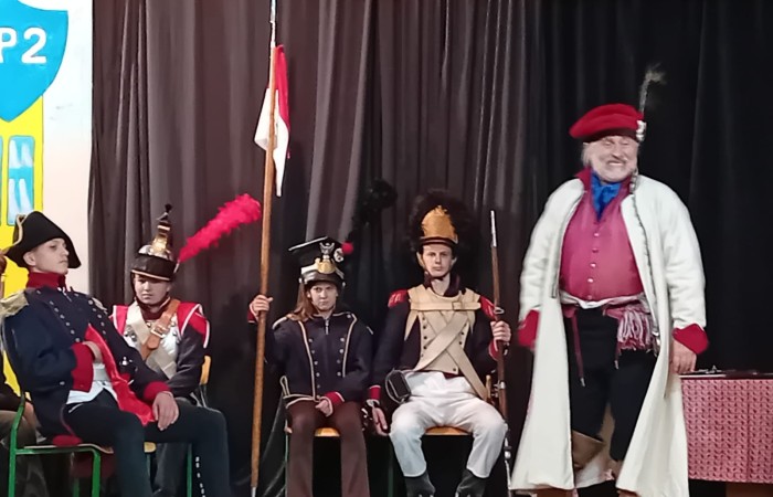 Każdego roku uczniowie naszej szkoły mają niepowtarzalną okazję wziąć udział w wyjątkowym wydarzeniu edukacyjnym - ŻYWEJ LEKCJI HISTORII, prowadzonej przez grupę rekonstrukcyjną Chorągiew Komturstwa Gniewskiego. To spotkanie, które na długo pozostaje w pamięci uczestników, łącząc wiedzę historyczną z emocjami, ruchem i bezpośrednim kontaktem z przeszłością.
W tym roku tematyka spotkań została zrealizowana na dwóch poziomach wiekowych:
Klasy 4-6: Świat starożytnych Greków i Rzymian
Uczniowie klas młodszych przenieśli się do czasów starożytności - epoki potężnych cywilizacji, mitologii, igrzysk olimpijskich i legionów rzymskich. Dzięki strojom z epoki, realistycznym rekwizytom i barwnym opowieściom rekonstruktorów, dzieci mogły poczuć atmosferę antycznego świata. Dowiedzieli się, jak wyglądało życie codzienne Greków i Rzymian, jakie były zwyczaje wojenne, a nawet jak wyglądały ćwiczenia wojskowe legionistów. Zajęcia - prowadzone w formie interaktywnej - dały uczniom możliwość przymierzenia elementów uzbrojenia oraz wzięcia udziału w krótkich pokazach.
Klasy 7-8: Długi wiek XIX
Starsze klasy uczestniczyły w lekcji poświęconej Długiemu wiekowi XIX, czyli okresowi, który ukształtował współczesny świat. Rekonstruktorzy przybliżyli wydarzenia związane z rewolucjami, walką o niepodległość, przemianami społecznymi i narodzinami nowoczesnych idei. Szczególną uwagę poświęcono wydarzeniom ważnym dla Polski - rozbiorom, powstaniom narodowym i postaciom kluczowym dla naszej historii. Uczniowie mogli zobaczyć repliki broni, a także stroje z XIX wieku. Dla wielu była to okazja do poznania historii w sposób bardziej angażujący niż podręcznik - przez opowieści, prezentacje multimedialne i inscenizacje.
Żywa lekcja historii to nie tylko atrakcja, ale przede wszystkim cenna forma nauki. Bezpośredni kontakt z pasjonatami historii oraz aktywne uczestnictwo w przedsięwzięciu sprawia, że uczniowie lepiej zapamiętują materiał, rozbudzają swoją ciekawość i rozwijają szacunek do dziedzictwa kulturowego.