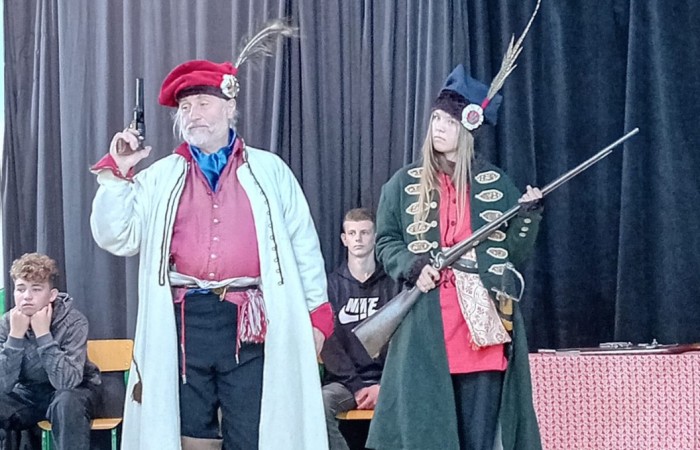 Każdego roku uczniowie naszej szkoły mają niepowtarzalną okazję wziąć udział w wyjątkowym wydarzeniu edukacyjnym - ŻYWEJ LEKCJI HISTORII, prowadzonej przez grupę rekonstrukcyjną Chorągiew Komturstwa Gniewskiego. To spotkanie, które na długo pozostaje w pamięci uczestników, łącząc wiedzę historyczną z emocjami, ruchem i bezpośrednim kontaktem z przeszłością.
W tym roku tematyka spotkań została zrealizowana na dwóch poziomach wiekowych:
Klasy 4-6: Świat starożytnych Greków i Rzymian
Uczniowie klas młodszych przenieśli się do czasów starożytności - epoki potężnych cywilizacji, mitologii, igrzysk olimpijskich i legionów rzymskich. Dzięki strojom z epoki, realistycznym rekwizytom i barwnym opowieściom rekonstruktorów, dzieci mogły poczuć atmosferę antycznego świata. Dowiedzieli się, jak wyglądało życie codzienne Greków i Rzymian, jakie były zwyczaje wojenne, a nawet jak wyglądały ćwiczenia wojskowe legionistów. Zajęcia - prowadzone w formie interaktywnej - dały uczniom możliwość przymierzenia elementów uzbrojenia oraz wzięcia udziału w krótkich pokazach.
Klasy 7-8: Długi wiek XIX
Starsze klasy uczestniczyły w lekcji poświęconej Długiemu wiekowi XIX, czyli okresowi, który ukształtował współczesny świat. Rekonstruktorzy przybliżyli wydarzenia związane z rewolucjami, walką o niepodległość, przemianami społecznymi i narodzinami nowoczesnych idei. Szczególną uwagę poświęcono wydarzeniom ważnym dla Polski - rozbiorom, powstaniom narodowym i postaciom kluczowym dla naszej historii. Uczniowie mogli zobaczyć repliki broni, a także stroje z XIX wieku. Dla wielu była to okazja do poznania historii w sposób bardziej angażujący niż podręcznik - przez opowieści, prezentacje multimedialne i inscenizacje.
Żywa lekcja historii to nie tylko atrakcja, ale przede wszystkim cenna forma nauki. Bezpośredni kontakt z pasjonatami historii oraz aktywne uczestnictwo w przedsięwzięciu sprawia, że uczniowie lepiej zapamiętują materiał, rozbudzają swoją ciekawość i rozwijają szacunek do dziedzictwa kulturowego.