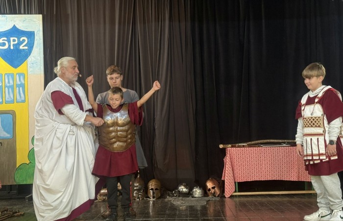 Każdego roku uczniowie naszej szkoły mają niepowtarzalną okazję wziąć udział w wyjątkowym wydarzeniu edukacyjnym - ŻYWEJ LEKCJI HISTORII, prowadzonej przez grupę rekonstrukcyjną Chorągiew Komturstwa Gniewskiego. To spotkanie, które na długo pozostaje w pamięci uczestników, łącząc wiedzę historyczną z emocjami, ruchem i bezpośrednim kontaktem z przeszłością.
W tym roku tematyka spotkań została zrealizowana na dwóch poziomach wiekowych:
Klasy 4-6: Świat starożytnych Greków i Rzymian
Uczniowie klas młodszych przenieśli się do czasów starożytności - epoki potężnych cywilizacji, mitologii, igrzysk olimpijskich i legionów rzymskich. Dzięki strojom z epoki, realistycznym rekwizytom i barwnym opowieściom rekonstruktorów, dzieci mogły poczuć atmosferę antycznego świata. Dowiedzieli się, jak wyglądało życie codzienne Greków i Rzymian, jakie były zwyczaje wojenne, a nawet jak wyglądały ćwiczenia wojskowe legionistów. Zajęcia - prowadzone w formie interaktywnej - dały uczniom możliwość przymierzenia elementów uzbrojenia oraz wzięcia udziału w krótkich pokazach.
Klasy 7-8: Długi wiek XIX
Starsze klasy uczestniczyły w lekcji poświęconej Długiemu wiekowi XIX, czyli okresowi, który ukształtował współczesny świat. Rekonstruktorzy przybliżyli wydarzenia związane z rewolucjami, walką o niepodległość, przemianami społecznymi i narodzinami nowoczesnych idei. Szczególną uwagę poświęcono wydarzeniom ważnym dla Polski - rozbiorom, powstaniom narodowym i postaciom kluczowym dla naszej historii. Uczniowie mogli zobaczyć repliki broni, a także stroje z XIX wieku. Dla wielu była to okazja do poznania historii w sposób bardziej angażujący niż podręcznik - przez opowieści, prezentacje multimedialne i inscenizacje.
Żywa lekcja historii to nie tylko atrakcja, ale przede wszystkim cenna forma nauki. Bezpośredni kontakt z pasjonatami historii oraz aktywne uczestnictwo w przedsięwzięciu sprawia, że uczniowie lepiej zapamiętują materiał, rozbudzają swoją ciekawość i rozwijają szacunek do dziedzictwa kulturowego.