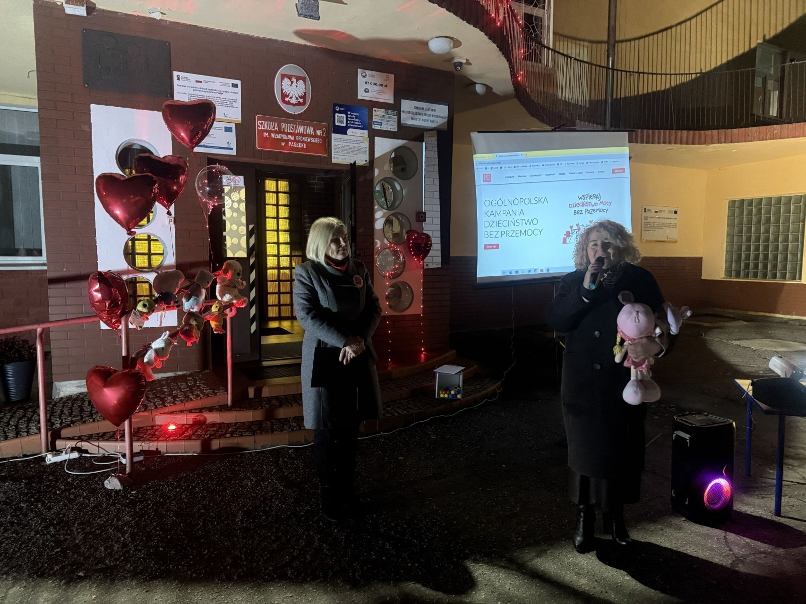 O godzinie 17:00 pod szkołą rozpoczęła się impreza, która zgromadziła około 200 osób. Szkoła została podświetlona na czerwono, co symbolizowało naszą jedność w walce z przemocą. Był to akcent podsumowujący nasze wcześ iej sze  działania w ramach Kampanii Ogólnopolskiej „Dzieciństwo bez Przemocy”. Od października uczniowie uczestniczyli w lekcjach online przygotowanych przez Fundację Dajemy Dzieciom Siłę. Rodzice również zostali objęci wsparciem w postaci webinaru online ww. fudacji.
Uczestnicy mogli wziąć udział w wspólnym śpiewaniu, quizie wiedzy o przemocy oraz tworzeniu „kamieni mocy” – symboli pozytywnej energii i wsparcia. Dodatkowo, w ramach konkursów, przyznano nagrody ufundowane przez Urząd Miejski w Pasłęku.
Ten cudowny czas umilił nam smaczny poczęstunek, w tym grochówka, pizza i ciasta, gorąca kawa i herbatka przygotowany przez panie kucharki i rodziców.
W wydarzeniu uczestniczyli również zaproszeni goście, w tym Burmistrz Pasłęka – pani Elżbieta Wasiuk,  podinspektor KP Pasłęk – pani Agnieszka Bielewicz - Piechowiak oraz przedstawiciel Kuratorium Oświaty w Elblągu – pani Teresa Bednarz, którzy wspierają nasze działania. Ich obecność była dowodem na to, jak ważna jest współpraca lokalnej społeczności w walce z przemocą wobec dzieci. Dziękujemy wszystkim, którzy wzięli udział w tym wyjątkowym dniu oraz przyczynili się do jego organizacji. Razem możemy stworzyć bezpieczne i przyjazne środowisko dla naszych dzieci!
