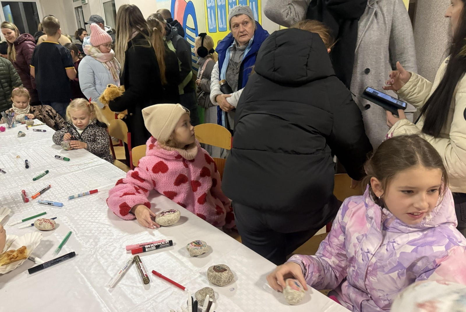 O godzinie 17:00 pod szkołą rozpoczęła się impreza, która zgromadziła około 200 osób. Szkoła została podświetlona na czerwono, co symbolizowało naszą jedność w walce z przemocą. Był to akcent podsumowujący nasze wcześ iej sze  działania w ramach Kampanii Ogólnopolskiej „Dzieciństwo bez Przemocy”. Od października uczniowie uczestniczyli w lekcjach online przygotowanych przez Fundację Dajemy Dzieciom Siłę. Rodzice również zostali objęci wsparciem w postaci webinaru online ww. fudacji.
Uczestnicy mogli wziąć udział w wspólnym śpiewaniu, quizie wiedzy o przemocy oraz tworzeniu „kamieni mocy” – symboli pozytywnej energii i wsparcia. Dodatkowo, w ramach konkursów, przyznano nagrody ufundowane przez Urząd Miejski w Pasłęku.
Ten cudowny czas umilił nam smaczny poczęstunek, w tym grochówka, pizza i ciasta, gorąca kawa i herbatka przygotowany przez panie kucharki i rodziców.
W wydarzeniu uczestniczyli również zaproszeni goście, w tym Burmistrz Pasłęka – pani Elżbieta Wasiuk,  podinspektor KP Pasłęk – pani Agnieszka Bielewicz - Piechowiak oraz przedstawiciel Kuratorium Oświaty w Elblągu – pani Teresa Bednarz, którzy wspierają nasze działania. Ich obecność była dowodem na to, jak ważna jest współpraca lokalnej społeczności w walce z przemocą wobec dzieci. Dziękujemy wszystkim, którzy wzięli udział w tym wyjątkowym dniu oraz przyczynili się do jego organizacji. Razem możemy stworzyć bezpieczne i przyjazne środowisko dla naszych dzieci!
