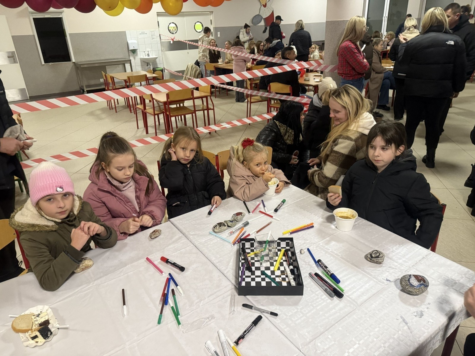 O godzinie 17:00 pod szkołą rozpoczęła się impreza, która zgromadziła około 200 osób. Szkoła została podświetlona na czerwono, co symbolizowało naszą jedność w walce z przemocą. Był to akcent podsumowujący nasze wcześ iej sze  działania w ramach Kampanii Ogólnopolskiej „Dzieciństwo bez Przemocy”. Od października uczniowie uczestniczyli w lekcjach online przygotowanych przez Fundację Dajemy Dzieciom Siłę. Rodzice również zostali objęci wsparciem w postaci webinaru online ww. fudacji.
Uczestnicy mogli wziąć udział w wspólnym śpiewaniu, quizie wiedzy o przemocy oraz tworzeniu „kamieni mocy” – symboli pozytywnej energii i wsparcia. Dodatkowo, w ramach konkursów, przyznano nagrody ufundowane przez Urząd Miejski w Pasłęku.
Ten cudowny czas umilił nam smaczny poczęstunek, w tym grochówka, pizza i ciasta, gorąca kawa i herbatka przygotowany przez panie kucharki i rodziców.
W wydarzeniu uczestniczyli również zaproszeni goście, w tym Burmistrz Pasłęka – pani Elżbieta Wasiuk,  podinspektor KP Pasłęk – pani Agnieszka Bielewicz - Piechowiak oraz przedstawiciel Kuratorium Oświaty w Elblągu – pani Teresa Bednarz, którzy wspierają nasze działania. Ich obecność była dowodem na to, jak ważna jest współpraca lokalnej społeczności w walce z przemocą wobec dzieci. Dziękujemy wszystkim, którzy wzięli udział w tym wyjątkowym dniu oraz przyczynili się do jego organizacji. Razem możemy stworzyć bezpieczne i przyjazne środowisko dla naszych dzieci!
