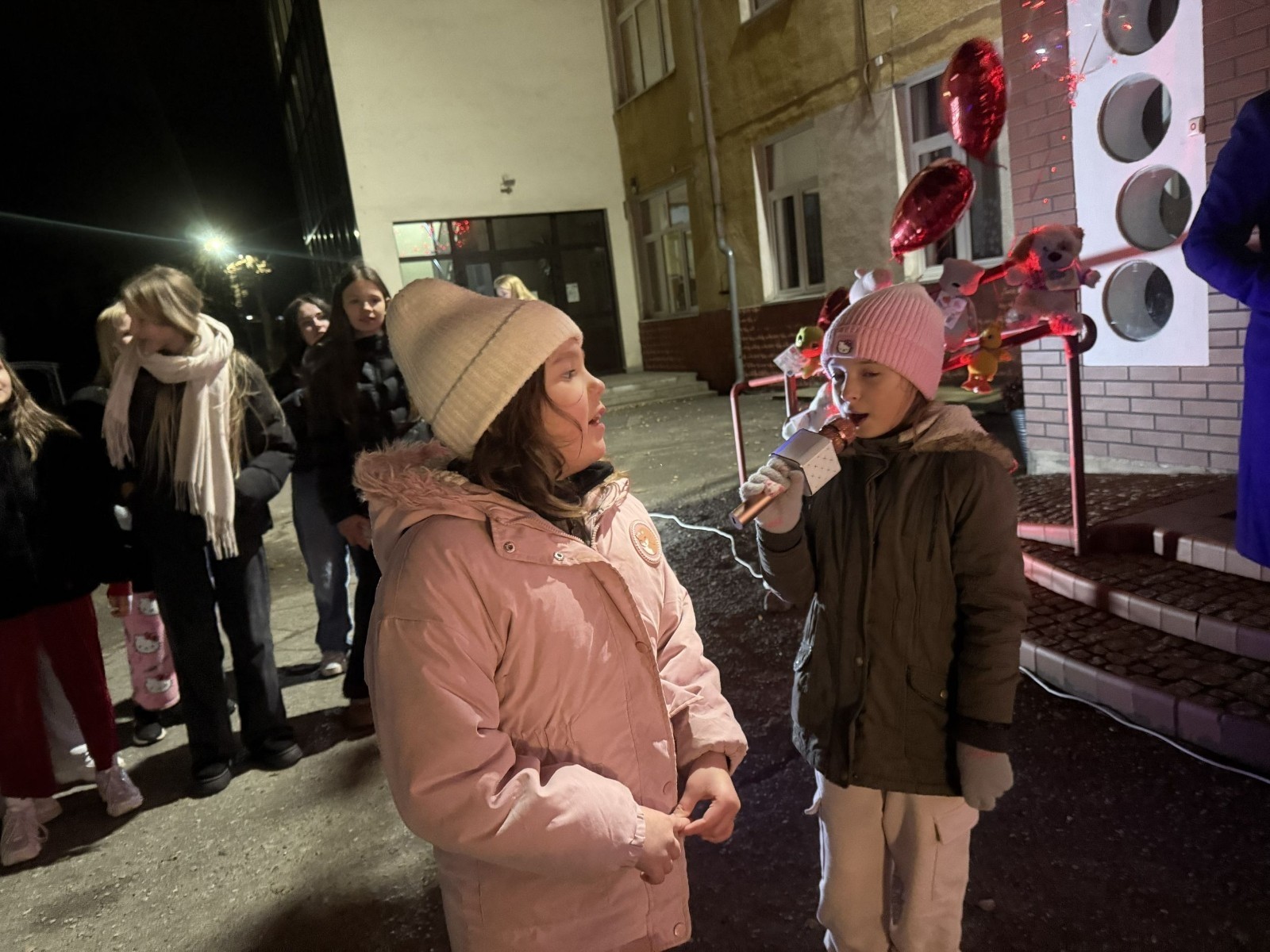 O godzinie 17:00 pod szkołą rozpoczęła się impreza, która zgromadziła około 200 osób. Szkoła została podświetlona na czerwono, co symbolizowało naszą jedność w walce z przemocą. Był to akcent podsumowujący nasze wcześ iej sze  działania w ramach Kampanii Ogólnopolskiej „Dzieciństwo bez Przemocy”. Od października uczniowie uczestniczyli w lekcjach online przygotowanych przez Fundację Dajemy Dzieciom Siłę. Rodzice również zostali objęci wsparciem w postaci webinaru online ww. fudacji.
Uczestnicy mogli wziąć udział w wspólnym śpiewaniu, quizie wiedzy o przemocy oraz tworzeniu „kamieni mocy” – symboli pozytywnej energii i wsparcia. Dodatkowo, w ramach konkursów, przyznano nagrody ufundowane przez Urząd Miejski w Pasłęku.
Ten cudowny czas umilił nam smaczny poczęstunek, w tym grochówka, pizza i ciasta, gorąca kawa i herbatka przygotowany przez panie kucharki i rodziców.
W wydarzeniu uczestniczyli również zaproszeni goście, w tym Burmistrz Pasłęka – pani Elżbieta Wasiuk,  podinspektor KP Pasłęk – pani Agnieszka Bielewicz - Piechowiak oraz przedstawiciel Kuratorium Oświaty w Elblągu – pani Teresa Bednarz, którzy wspierają nasze działania. Ich obecność była dowodem na to, jak ważna jest współpraca lokalnej społeczności w walce z przemocą wobec dzieci. Dziękujemy wszystkim, którzy wzięli udział w tym wyjątkowym dniu oraz przyczynili się do jego organizacji. Razem możemy stworzyć bezpieczne i przyjazne środowisko dla naszych dzieci!
