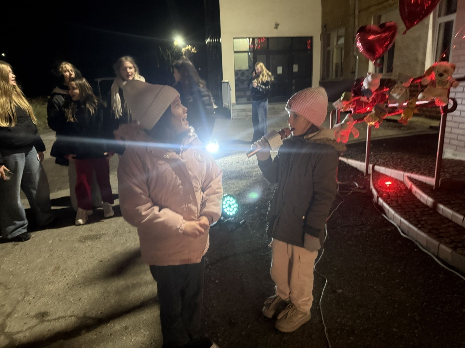 O godzinie 17:00 pod szkołą rozpoczęła się impreza, która zgromadziła około 200 osób. Szkoła została podświetlona na czerwono, co symbolizowało naszą jedność w walce z przemocą. Był to akcent podsumowujący nasze wcześ iej sze  działania w ramach Kampanii Ogólnopolskiej „Dzieciństwo bez Przemocy”. Od października uczniowie uczestniczyli w lekcjach online przygotowanych przez Fundację Dajemy Dzieciom Siłę. Rodzice również zostali objęci wsparciem w postaci webinaru online ww. fudacji.
Uczestnicy mogli wziąć udział w wspólnym śpiewaniu, quizie wiedzy o przemocy oraz tworzeniu „kamieni mocy” – symboli pozytywnej energii i wsparcia. Dodatkowo, w ramach konkursów, przyznano nagrody ufundowane przez Urząd Miejski w Pasłęku.
Ten cudowny czas umilił nam smaczny poczęstunek, w tym grochówka, pizza i ciasta, gorąca kawa i herbatka przygotowany przez panie kucharki i rodziców.
W wydarzeniu uczestniczyli również zaproszeni goście, w tym Burmistrz Pasłęka – pani Elżbieta Wasiuk,  podinspektor KP Pasłęk – pani Agnieszka Bielewicz - Piechowiak oraz przedstawiciel Kuratorium Oświaty w Elblągu – pani Teresa Bednarz, którzy wspierają nasze działania. Ich obecność była dowodem na to, jak ważna jest współpraca lokalnej społeczności w walce z przemocą wobec dzieci. Dziękujemy wszystkim, którzy wzięli udział w tym wyjątkowym dniu oraz przyczynili się do jego organizacji. Razem możemy stworzyć bezpieczne i przyjazne środowisko dla naszych dzieci!
