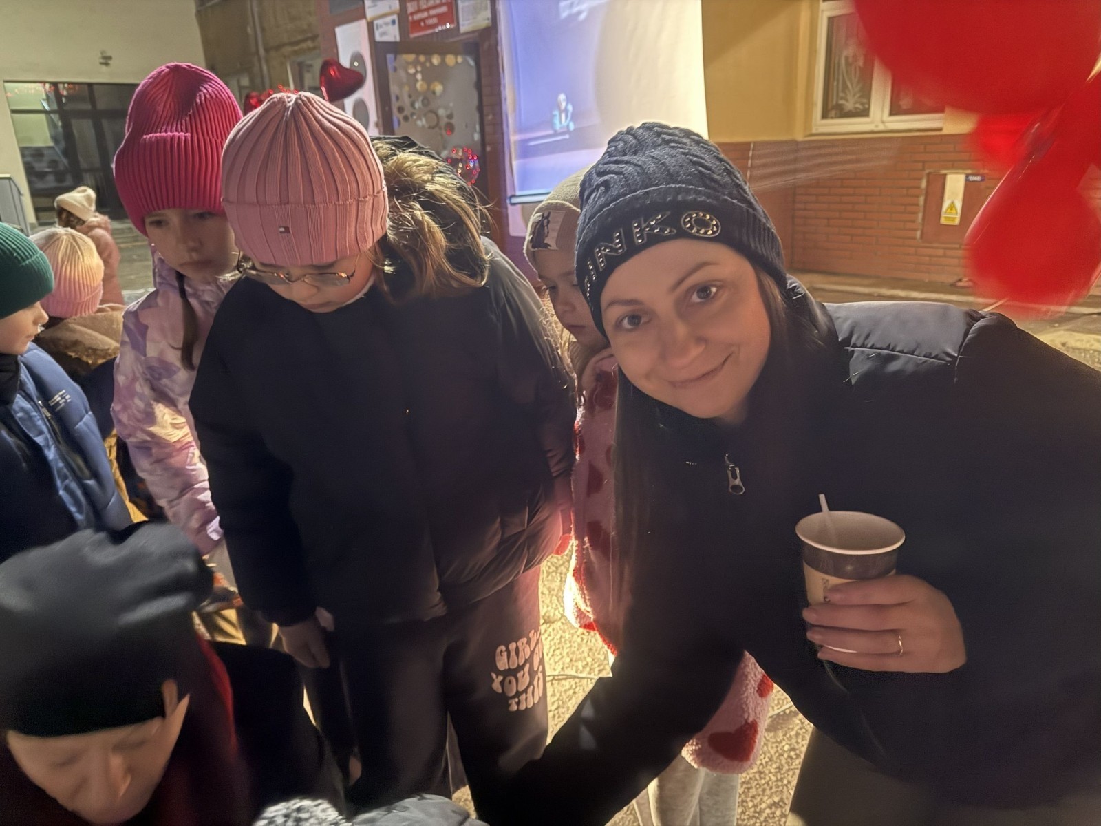 O godzinie 17:00 pod szkołą rozpoczęła się impreza, która zgromadziła około 200 osób. Szkoła została podświetlona na czerwono, co symbolizowało naszą jedność w walce z przemocą. Był to akcent podsumowujący nasze wcześ iej sze  działania w ramach Kampanii Ogólnopolskiej „Dzieciństwo bez Przemocy”. Od października uczniowie uczestniczyli w lekcjach online przygotowanych przez Fundację Dajemy Dzieciom Siłę. Rodzice również zostali objęci wsparciem w postaci webinaru online ww. fudacji.
Uczestnicy mogli wziąć udział w wspólnym śpiewaniu, quizie wiedzy o przemocy oraz tworzeniu „kamieni mocy” – symboli pozytywnej energii i wsparcia. Dodatkowo, w ramach konkursów, przyznano nagrody ufundowane przez Urząd Miejski w Pasłęku.
Ten cudowny czas umilił nam smaczny poczęstunek, w tym grochówka, pizza i ciasta, gorąca kawa i herbatka przygotowany przez panie kucharki i rodziców.
W wydarzeniu uczestniczyli również zaproszeni goście, w tym Burmistrz Pasłęka – pani Elżbieta Wasiuk,  podinspektor KP Pasłęk – pani Agnieszka Bielewicz - Piechowiak oraz przedstawiciel Kuratorium Oświaty w Elblągu – pani Teresa Bednarz, którzy wspierają nasze działania. Ich obecność była dowodem na to, jak ważna jest współpraca lokalnej społeczności w walce z przemocą wobec dzieci. Dziękujemy wszystkim, którzy wzięli udział w tym wyjątkowym dniu oraz przyczynili się do jego organizacji. Razem możemy stworzyć bezpieczne i przyjazne środowisko dla naszych dzieci!
