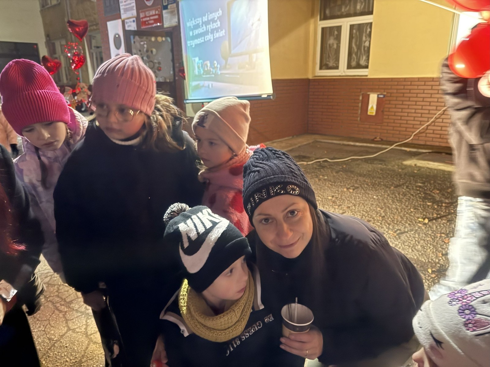 O godzinie 17:00 pod szkołą rozpoczęła się impreza, która zgromadziła około 200 osób. Szkoła została podświetlona na czerwono, co symbolizowało naszą jedność w walce z przemocą. Był to akcent podsumowujący nasze wcześ iej sze  działania w ramach Kampanii Ogólnopolskiej „Dzieciństwo bez Przemocy”. Od października uczniowie uczestniczyli w lekcjach online przygotowanych przez Fundację Dajemy Dzieciom Siłę. Rodzice również zostali objęci wsparciem w postaci webinaru online ww. fudacji.
Uczestnicy mogli wziąć udział w wspólnym śpiewaniu, quizie wiedzy o przemocy oraz tworzeniu „kamieni mocy” – symboli pozytywnej energii i wsparcia. Dodatkowo, w ramach konkursów, przyznano nagrody ufundowane przez Urząd Miejski w Pasłęku.
Ten cudowny czas umilił nam smaczny poczęstunek, w tym grochówka, pizza i ciasta, gorąca kawa i herbatka przygotowany przez panie kucharki i rodziców.
W wydarzeniu uczestniczyli również zaproszeni goście, w tym Burmistrz Pasłęka – pani Elżbieta Wasiuk,  podinspektor KP Pasłęk – pani Agnieszka Bielewicz - Piechowiak oraz przedstawiciel Kuratorium Oświaty w Elblągu – pani Teresa Bednarz, którzy wspierają nasze działania. Ich obecność była dowodem na to, jak ważna jest współpraca lokalnej społeczności w walce z przemocą wobec dzieci. Dziękujemy wszystkim, którzy wzięli udział w tym wyjątkowym dniu oraz przyczynili się do jego organizacji. Razem możemy stworzyć bezpieczne i przyjazne środowisko dla naszych dzieci!
