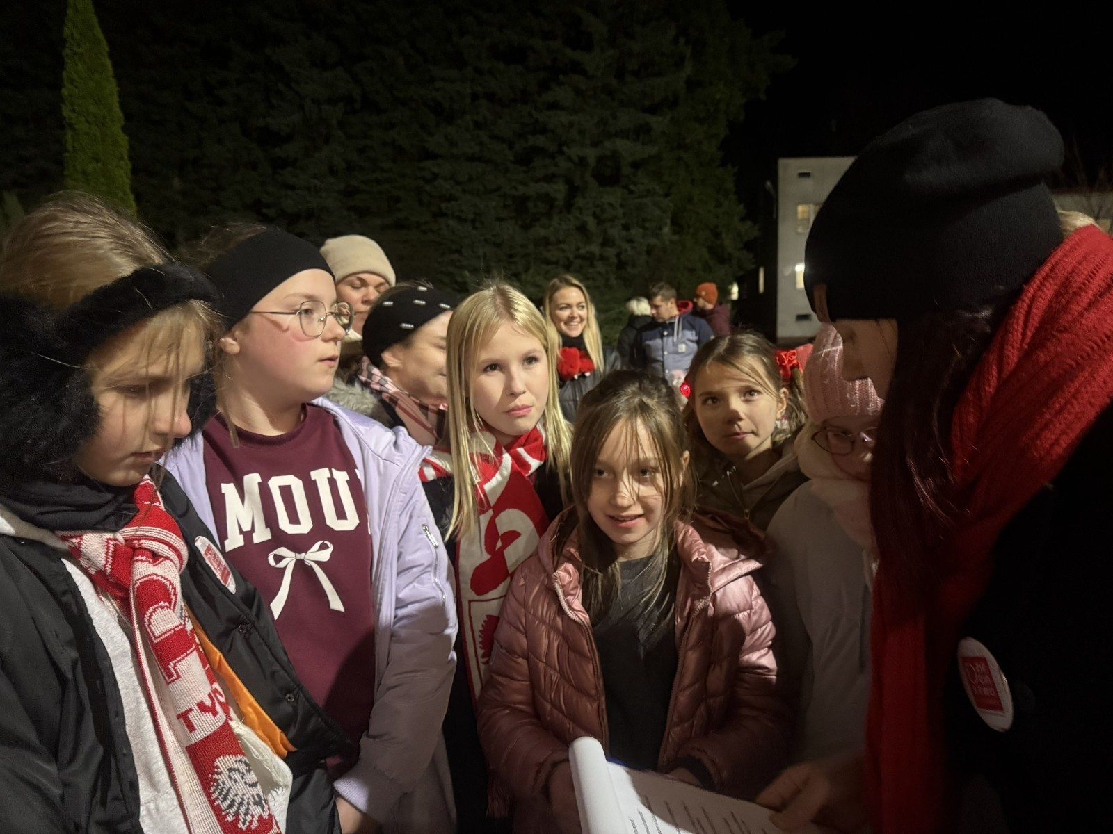 O godzinie 17:00 pod szkołą rozpoczęła się impreza, która zgromadziła około 200 osób. Szkoła została podświetlona na czerwono, co symbolizowało naszą jedność w walce z przemocą. Był to akcent podsumowujący nasze wcześ iej sze  działania w ramach Kampanii Ogólnopolskiej „Dzieciństwo bez Przemocy”. Od października uczniowie uczestniczyli w lekcjach online przygotowanych przez Fundację Dajemy Dzieciom Siłę. Rodzice również zostali objęci wsparciem w postaci webinaru online ww. fudacji.
Uczestnicy mogli wziąć udział w wspólnym śpiewaniu, quizie wiedzy o przemocy oraz tworzeniu „kamieni mocy” – symboli pozytywnej energii i wsparcia. Dodatkowo, w ramach konkursów, przyznano nagrody ufundowane przez Urząd Miejski w Pasłęku.
Ten cudowny czas umilił nam smaczny poczęstunek, w tym grochówka, pizza i ciasta, gorąca kawa i herbatka przygotowany przez panie kucharki i rodziców.
W wydarzeniu uczestniczyli również zaproszeni goście, w tym Burmistrz Pasłęka – pani Elżbieta Wasiuk,  podinspektor KP Pasłęk – pani Agnieszka Bielewicz - Piechowiak oraz przedstawiciel Kuratorium Oświaty w Elblągu – pani Teresa Bednarz, którzy wspierają nasze działania. Ich obecność była dowodem na to, jak ważna jest współpraca lokalnej społeczności w walce z przemocą wobec dzieci. Dziękujemy wszystkim, którzy wzięli udział w tym wyjątkowym dniu oraz przyczynili się do jego organizacji. Razem możemy stworzyć bezpieczne i przyjazne środowisko dla naszych dzieci!
