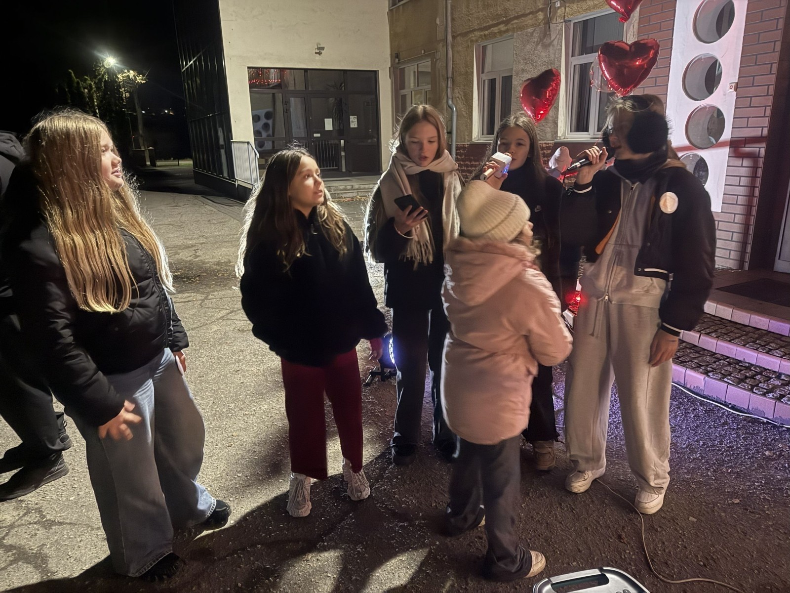 O godzinie 17:00 pod szkołą rozpoczęła się impreza, która zgromadziła około 200 osób. Szkoła została podświetlona na czerwono, co symbolizowało naszą jedność w walce z przemocą. Był to akcent podsumowujący nasze wcześ iej sze  działania w ramach Kampanii Ogólnopolskiej „Dzieciństwo bez Przemocy”. Od października uczniowie uczestniczyli w lekcjach online przygotowanych przez Fundację Dajemy Dzieciom Siłę. Rodzice również zostali objęci wsparciem w postaci webinaru online ww. fudacji.
Uczestnicy mogli wziąć udział w wspólnym śpiewaniu, quizie wiedzy o przemocy oraz tworzeniu „kamieni mocy” – symboli pozytywnej energii i wsparcia. Dodatkowo, w ramach konkursów, przyznano nagrody ufundowane przez Urząd Miejski w Pasłęku.
Ten cudowny czas umilił nam smaczny poczęstunek, w tym grochówka, pizza i ciasta, gorąca kawa i herbatka przygotowany przez panie kucharki i rodziców.
W wydarzeniu uczestniczyli również zaproszeni goście, w tym Burmistrz Pasłęka – pani Elżbieta Wasiuk,  podinspektor KP Pasłęk – pani Agnieszka Bielewicz - Piechowiak oraz przedstawiciel Kuratorium Oświaty w Elblągu – pani Teresa Bednarz, którzy wspierają nasze działania. Ich obecność była dowodem na to, jak ważna jest współpraca lokalnej społeczności w walce z przemocą wobec dzieci. Dziękujemy wszystkim, którzy wzięli udział w tym wyjątkowym dniu oraz przyczynili się do jego organizacji. Razem możemy stworzyć bezpieczne i przyjazne środowisko dla naszych dzieci!
